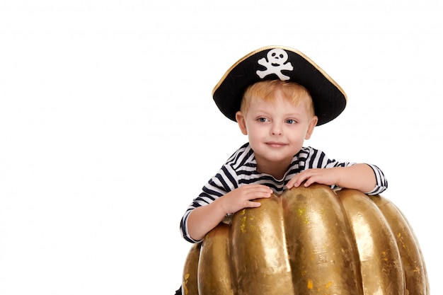 Drôle petit garçon en costumes de carnaval de pirates debout avec une grosse citrouille sur blanc