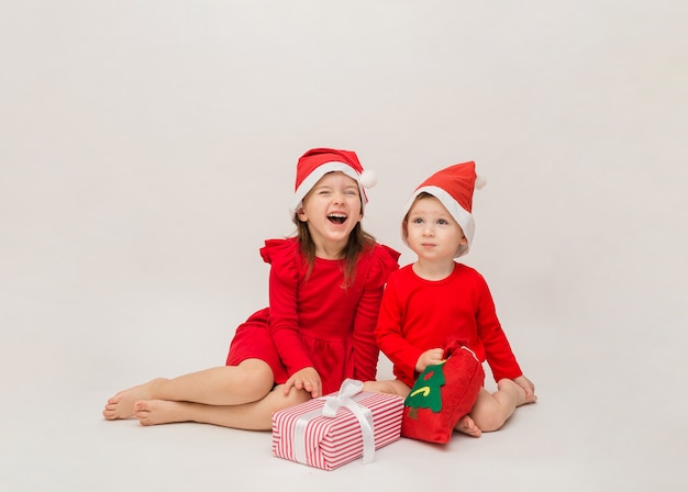 Drôle de petit garçon et fille en bonnets rouges avec des cadeaux de Noël sur un mur blanc avec un espace pour