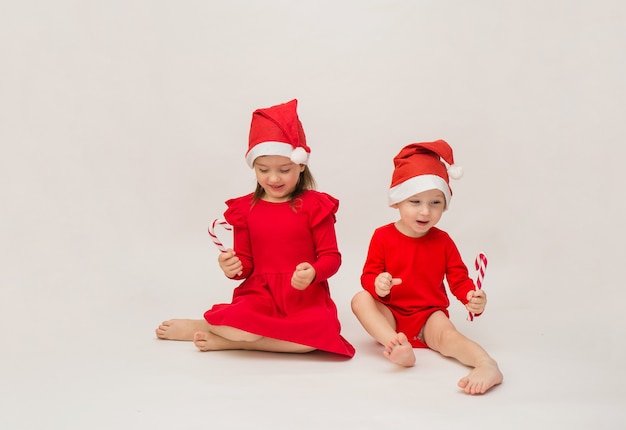 Drôle de petit garçon et fille en bonnets rouges avec des sucettes sur un mur blanc