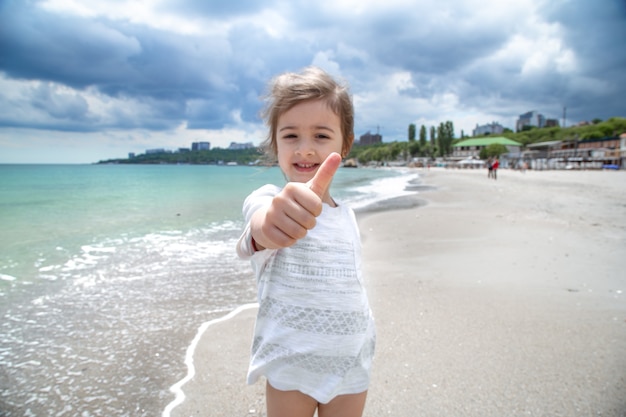 Drôle de petite fille au bord de la mer sourit et se penche sur la caméra.