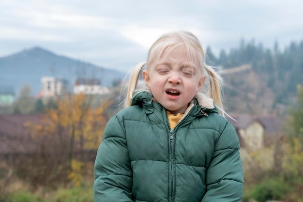 Drôle de petite fille blonde avec deux queues éternue debout dans l'air frais de la campagne Enfants froid en automne