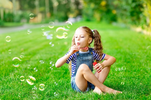 Drôle de petite fille en été sur la pelouse avec des bulles de savon sur l'herbe verte s'amusant et se réjouissant de l'espace pour le texte