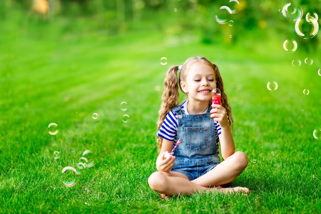 Drôle de petite fille en été sur la pelouse avec des bulles de savon sur l'herbe verte s'amusant et se réjouissant de l'espace pour le texte