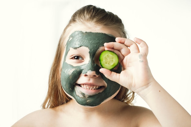 Drôle petite fille avec un masque cosmétique d&#39;argile dans une serviette de bain