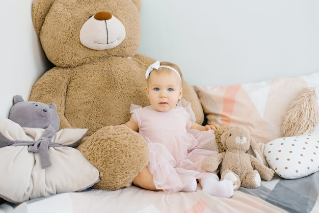 Drôle de petite fille mignonne de 1 an, assise sur le lit le matin avec un arc sur la tête.