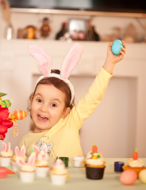 Drôle de petite fille portant des oreilles de lapin et peinture oeuf de Pâques au printemps à la maison.