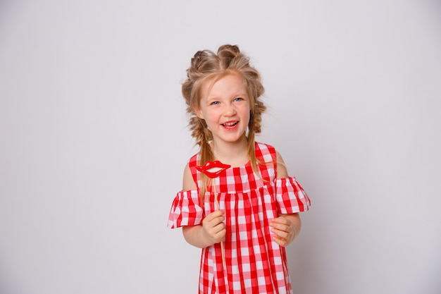 Drôle de robe d'été bébé fille souriante sur fond blanc. Petite fille avec un accessoire pour les lèvres sur un bâton.