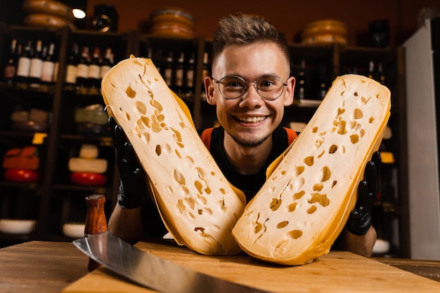 Drôle de sommelier au fromage fou avec 2 morceaux de maasdam naturel limité vieilli entre sa tête Travailleur créatif du magasin d'alimentation au fromage souriant en riant et en s'amusant