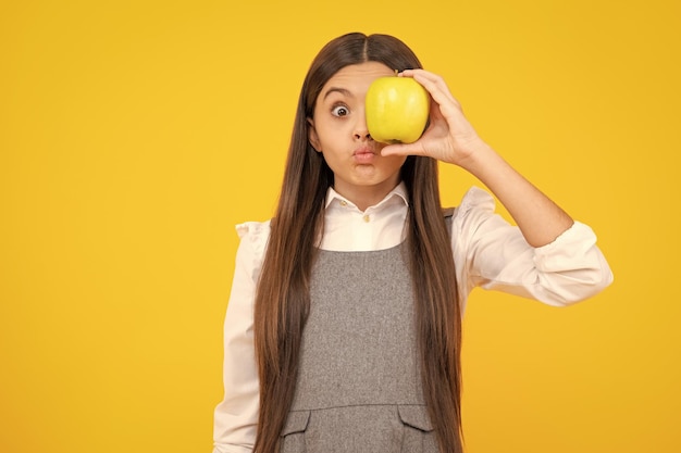 Drôle de visage Enfant fille mangeant une pomme sur fond jaune isolé Tennager avec des fruits