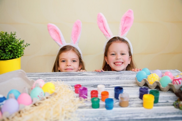 Drôles d'enfants filles dans des oreilles de lapin, jetant un coup d'œil derrière la table avec des oeufs de pâques colorés