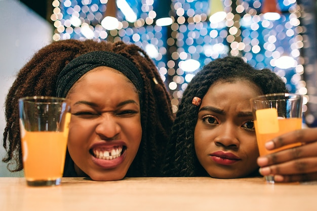 Drôles de jeunes femmes africaines gardent la tête sur la table. Le premier modèle rétrécit. Le second a l'air triste. Elle tient un verre de jus avec la main.
