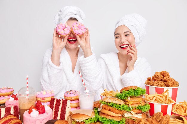 De drôles de jeunes femmes passent du temps libre à la maison et gardent de délicieux beignets sucrés sur les yeux entourés d'une délicieuse restauration rapide