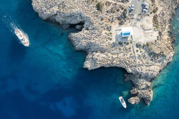 Photo drone aérien cap grecque péninsule agioi anargyroi église sur les rochers bateaux de croisière à la voile