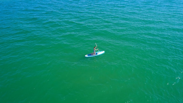 Drone aérien vue d'oiseau d'une jeune femme exerçant une planche de sup dans des eaux claires tropicales turquoises