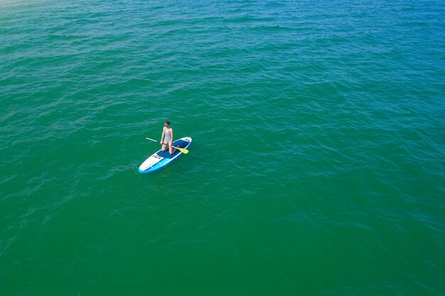 Drone aérien vue d'oiseau d'une jeune femme exerçant une planche de sup dans des eaux claires tropicales turquoises