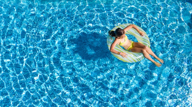 Drone aérien vue de petite fille dans la piscine d'en haut, enfant nage sur anneau gonflable beignet, enfant s'amuse dans l'eau bleue sur la station de vacances en famille