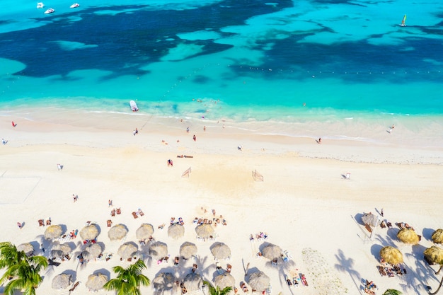 Drone vue sur la plage tropicale des Caraïbes avec parasols en paille, palmiers et bateaux