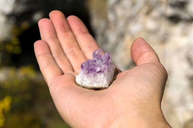 Druse de cristaux violets naturels non traités d'améthyste sur un morceau de roche sur la main