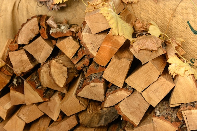 Photo du bois de chauffage sec avec des feuilles d'automne sur le dessus empilé à l'intérieur sur un vieux sac en toile