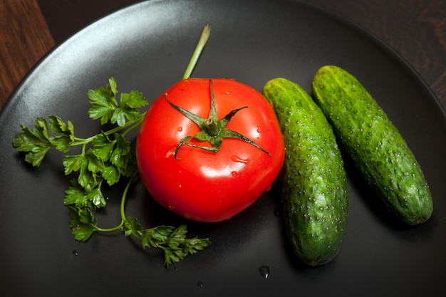 Photo du concombre de tomate rouge et du persil sur une assiette noire