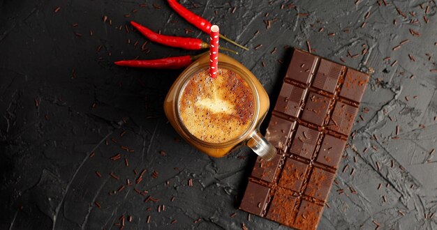 Du dessus du pot en verre avec café et paille sur table avec barre de chocolat et piment