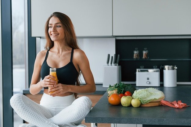 Avec du jus d'orange frais Jeune femme européenne est à l'intérieur à la cuisine à l'intérieur avec des aliments sains