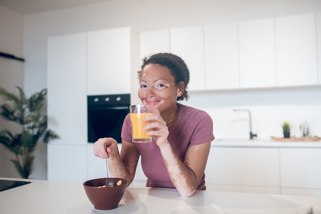 Du jus d'orange. Jeune femme à la peau foncée tenant un verre de jus d'orange