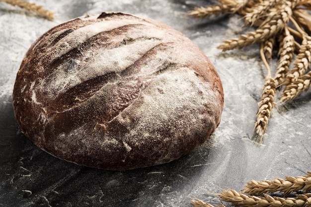 Du pain frais sur une table en gros plan dans une pincée de farine et d'épis de blé, mise au point sélective. Nourriture saine au levain et concept de boulangerie traditionnelle. Style campagnard