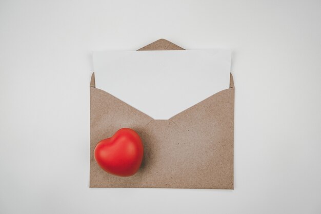 Du papier blanc vierge est placé sur l'enveloppe de papier brun ouverte avec un cœur rouge