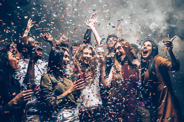 Photo du plaisir en mouvement. groupe de beaux jeunes jetant des confettis colorés tout en dansant et en ayant l'air heureux