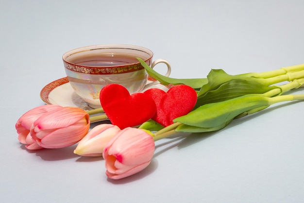 Du thé dans une tasse en porcelaine ancienne, un bouquet de tulipes roses, une paire de coeurs écarlates.