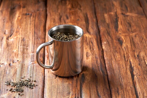 Du thé vert dans une tasse en acier inoxydable sur une vieille table en bois