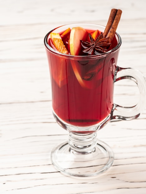 Du vin chaud avec des épices et des bâtons de cannelle se dresse sur une table en bois blanc.