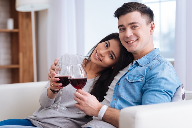 Du vin pour l'humeur. Couple exubérant vigoureux tenant des verres avec du vin tout en regardant la caméra