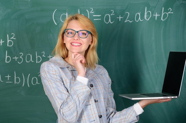 Éducateur dame intelligente avec un ordinateur portable moderne surfer sur fond de tableau sur Internet Une enseignante porte des lunettes tient un ordinateur portable surfer sur Internet Éducation scolaire de base Concept de technologies numériques