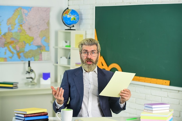 Éducateur intelligent mature Journée de la connaissance Homme enseignant assis dans la salle de classe Superviser le professeur surveiller et soutenir Plan de leçon Dossiers documentaires sur la paperasserie Devoirs scolaires Retour à l'école