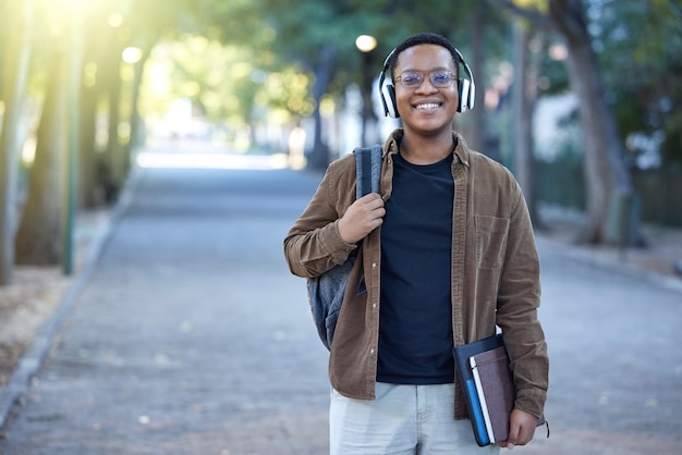 Éducation musicale et portrait d'un homme noir dans un parc pour une promenade apprenant et étudiant dans la nature Bonne université et étudiant africain avec des écouteurs pour l'audio tout en étant prêt à commencer l'université