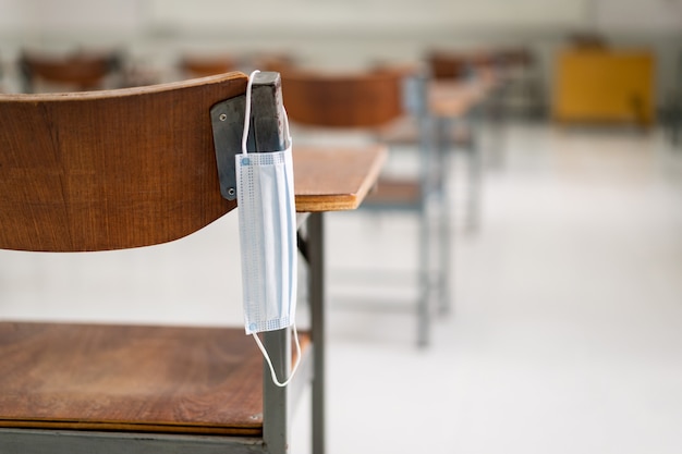 Éducation pendant COVID-19 : un masque médical usagé est suspendu à une chaise de conférence en bois dans une salle de classe vide pendant la pandémie de COVID-19
