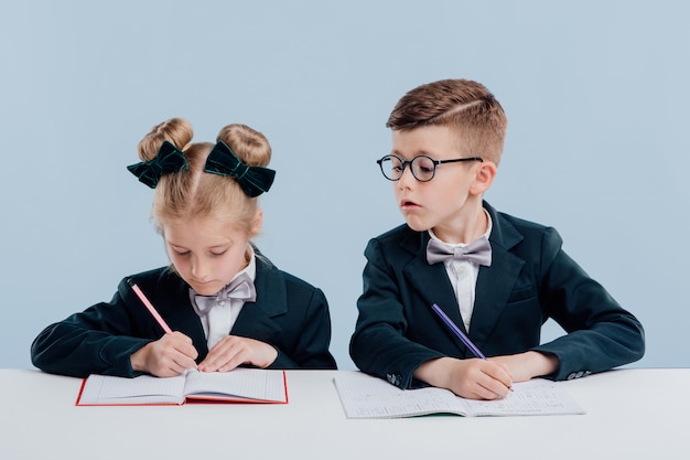 Éducation. petit garçon essayant de copier un papier test d'écolière, en uniforme scolaire, assis à la table blanche