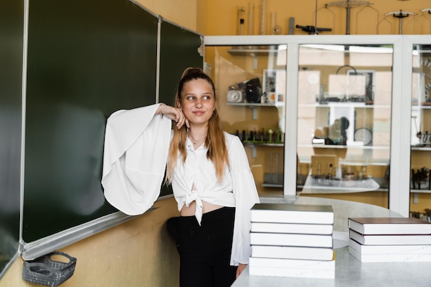 Éducation scolaire Écolière avec de nombreux livres posant au tableau noir dans la salle de classe Fille étudiant à l'école et se préparant aux examens