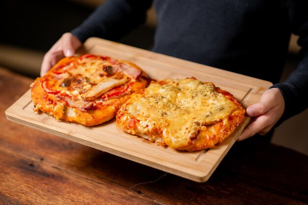 Un duo de petites pizzas faites maison tenues par des mains masculines sur une surface en bois