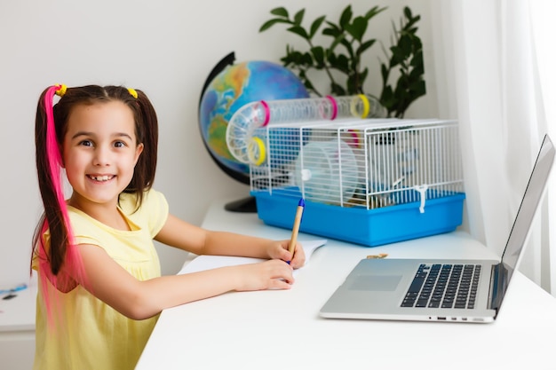 Éduquez à la maison. Une fillette fait ses devoirs avec un hamster pour animaux de compagnie. Hamster roux drôle assis sur une table où l'enfant écrit. Retour à l'école.