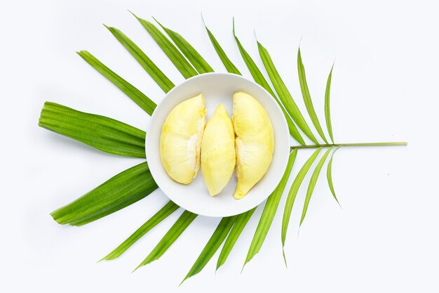 Durian en plaque blanche sur des feuilles de palmiers tropicaux sur fond blanc.