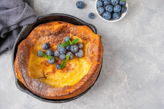 Dutch Baby pancake aux myrtilles fraîches à la menthe et saupoudré de sucre glace dans des poêles en fer