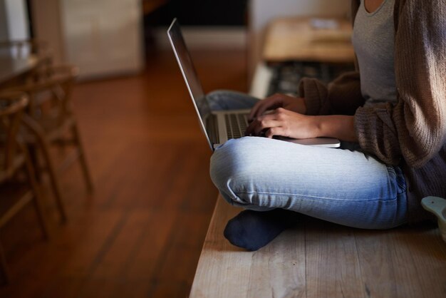 E-mails du matin Image recadrée d'une femme assise sur un comptoir en train de taper sur son ordinateur portable