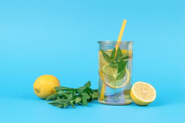 Eau au citron et à la menthe dans un verre avec un tube à cocktail sur fond bleu