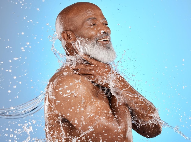 Photo eau de beauté et éclaboussures de nettoyage d'un homme âgé pour les soins du corps, l'hygiène et le mode de vie sain bonne douche et modèle noir mature lavant la peau au fond bleu du studio avec un sourire satisfait