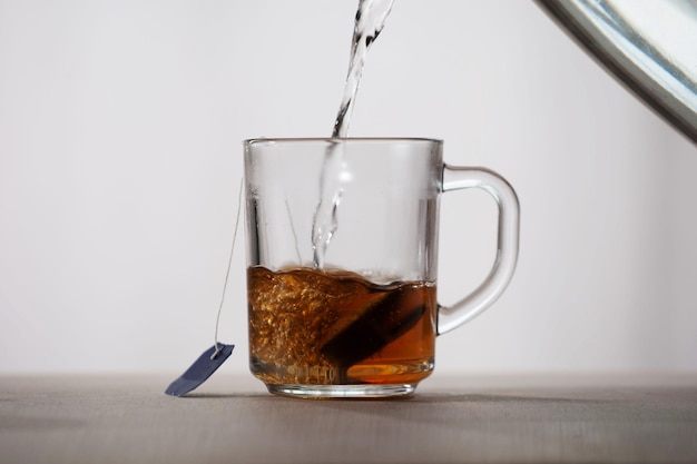 L'eau bouillante est versée dans une tasse en verre avec un sachet de thé