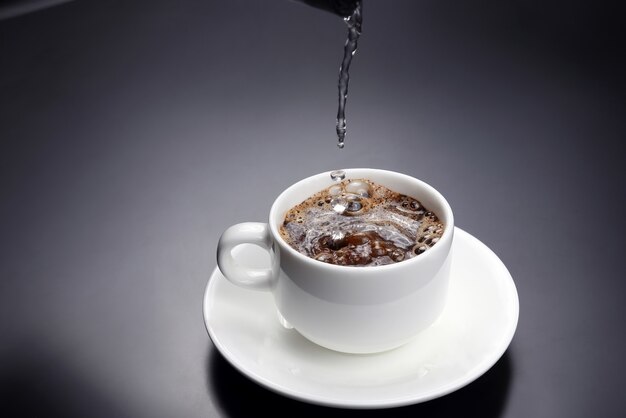 De l'eau bouillie est versée dans une tasse blanche avec du café noir