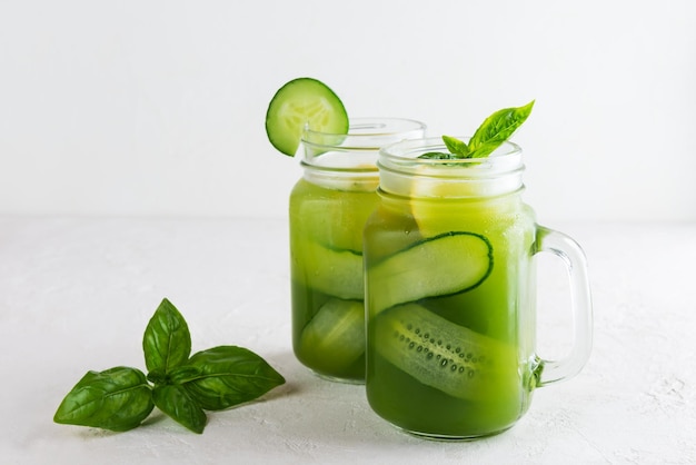 Eau de concombre au basilic et citron dans une tasse en verre sur table lumineuse